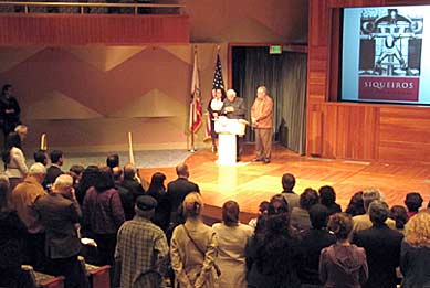 Close to 200 people filled the Los Angeles Central Library’s Mark Taper Auditorium to hear the latest news on the status of the Siqueiros mural project. In this photo, Father Richard Estrada of Our Lady Queen of Angels Catholic Church in Los Angeles, gives a benediction to open the event. Father Estrada blessed Siqueiros, and all artists who work for social justice. Photo/Mark Vallen ©.